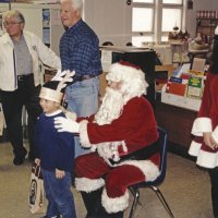 12-20-02 - Mission Education Center Christmas with Santa, Mission Education Center, San Francisco - A student poses with Santa after receiving his present. On the left, Joe Farrah and Al Gentile  pause their duties, and Santa’s assistant smiles for the camera.