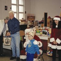 12-20-02 - Mission Education Center Christmas with Santa, Mission Education Center, San Francisco - A student happily poses with Santa after receiving his present. On the left, Joe Farrah and Al Gentile  pause their duties, and Santa’s assistant smiles for the camera.