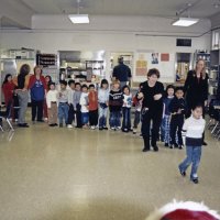 12-20-02 - Mission Education Center Christmas with Santa, Mission Education Center, San Francisco - Seventeen students all lined up and ready for Santa. The first just takes her first steps toward Santa. Her teachers and support staff look on; Deborah Molof, Principal is center right. Aaron Straus stand with back to camera in the back of the room.