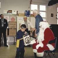 12-20-02 - Mission Education Center Christmas with Santa, Mission Education Center, San Francisco - A student can’t wait to see what Santa has brought him as his assistant looks on. In the background are. L to R, Dick Johnson, Steve Currier, Joe Farrah, and Al Gentile who just delivered a gift to Santa.
