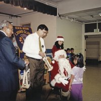 12-20-02 - Mission Education Center Christmas with Santa, Mission Education Center, San Francisco - Dr. Mehendra Dave, on left, and Sheriar Irani stand ready with gift bags while a student has a little talk with Santa.