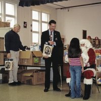 12-20-02 - Mission Education Center Christmas with Santa, Mission Education Center, San Francisco - Santa talks with a student as his assistant looks on. Aaron Straus, seated, Dick Johnson, and Steve Currier get gift bags ready on the left.