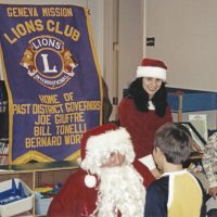 12-20-02 - Mission Education Center Christmas with Santa, Mission Education Center, San Francisco - Steve Currier, left, and Santa’s assistant look on as Santa talks with a student before presenting his with his gift; others wait on the right after receiving their gifts.