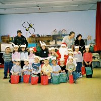 12/15/06 - Christmas at Mission Educational Center, Police Officer “Nacho” Martinez as Santa - Santa poses with a class as his Police Officer escorts, Lion Bob Fenech (light blue shirt), principal Deborah Molof (on Bob’s left), and others look on.