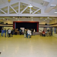 2/23/08 - 26th Annual Crab Feed - Janet Pomeroy Recreation & Rehabilitation Center, San Francisco - The first guests arriving and just standing around. Estelle Bottarini selling tickets in front of the sign; Charlie Bottarini on right edge of stage; Handford Clews (seated), LaVerne Cheso, and Dick Johnson to Charlie’s right. Covered trays of crab are on the right.