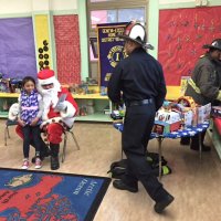 12-15-16 - Christmas with Santa with the help of Los Bomberos Firefighters, Mission Education Center, San Francisco - Santa looking over a student’s gift with her as Los Bomberos Firefighters handle the presents.