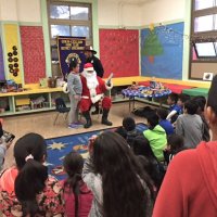 12-15-16 - Christmas with Santa with the help of Los Bomberos Firefighters, Mission Education Center, San Francisco - A students receives her gift from Santa as others look on.