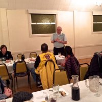 10/17/18 - District Governor's Visitation, Italian American Social Club - L to R outside far table: Lions Sharon Eberhardt, and visiting Aaron Straus from Daly City Host Lions. Inside far table: visiting Lion Hernaldo Martinez from Pedregal, Panama (in vest), and guest speaker Carla Vasquez. L to R near table Lion Bill Graziano, Lyle Workman, and Ward Donnelly (just peeking in.) Lion Aaron Straus filling us in on the history of the Mission Education Center project and introducing our guest speaker Carla Vasquez, Principal, MEC.