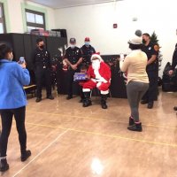 12-10-21 - Mission Education Center Christmas with Santa @ MEC, San Francisco - A shy little boy receives his gift from Santa as Los Bomberos Firefighters look on and teachers snap photos.