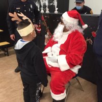 12-10-21 - Mission Education Center Christmas with Santa @ MEC, San Francisco - A little boy waits patiently to receive his gift from Santa as members of Los Bomberos Firefighters look on.