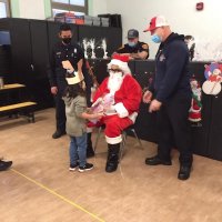 12-10-21 - Mission Education Center Christmas with Santa @ MEC, San Francisco - A little girl receives her gift from Santa as her teacher and members of Los Bomberos Firefighters look on.