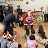 12-9-22 - Mission Education Center Christmas with Santa, San Francisco - A student, after receiving his gift from Santa, poses with it and Santa so a Los Bomberos member can snap a photo.