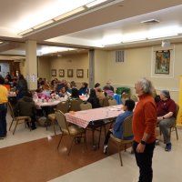 2-25-23 - 36th Annual Crab Feed - St. Philip the Apostle Church, San Francisco - On left in aisle are Bob Lawhon and Suzie Moy settling up a raffle ticket transaction; center right is Leona Wong and Bob Fenech (sitting), and Paul Corvi looking on.